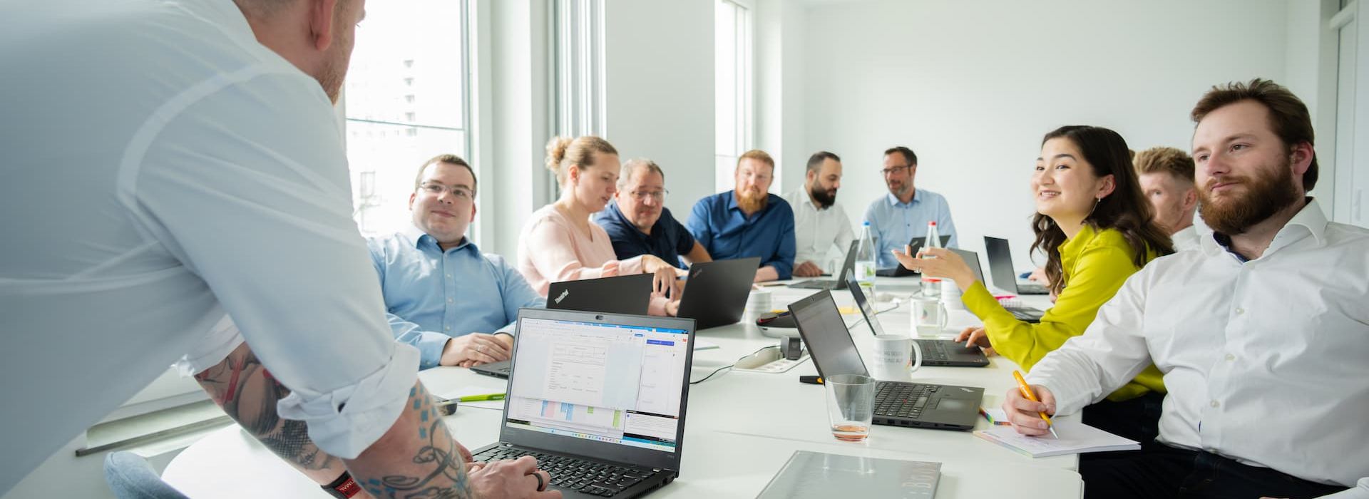 Trainer im Vordergrund, an einem Tisch mit Schulungsteilnehmern