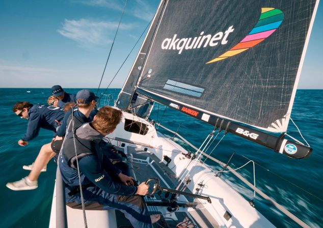 Junge Männer auf einem Segelboot auf dem Meer mit schwarzem Segel und buntem Logo